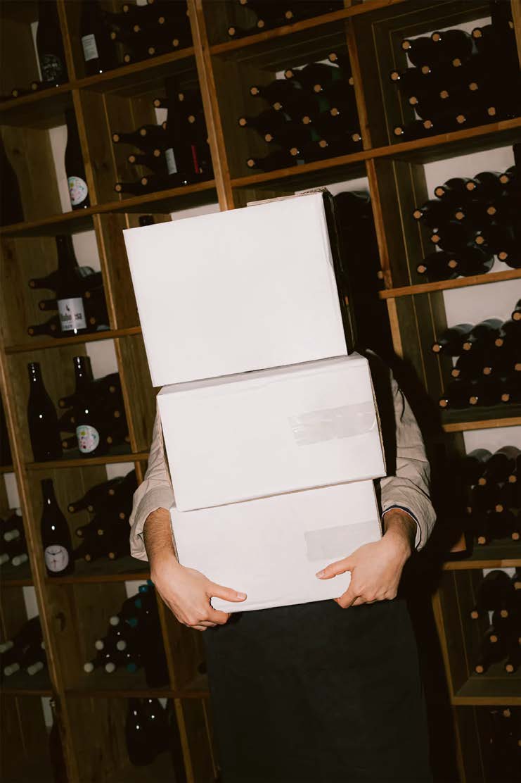 Warehouse operative carrying stacked boxes through a wine cellar at a drinks wholesaler